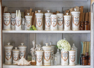 A collection of French apothecary jars is displayed on a shelf among sweet flowers and seashells.