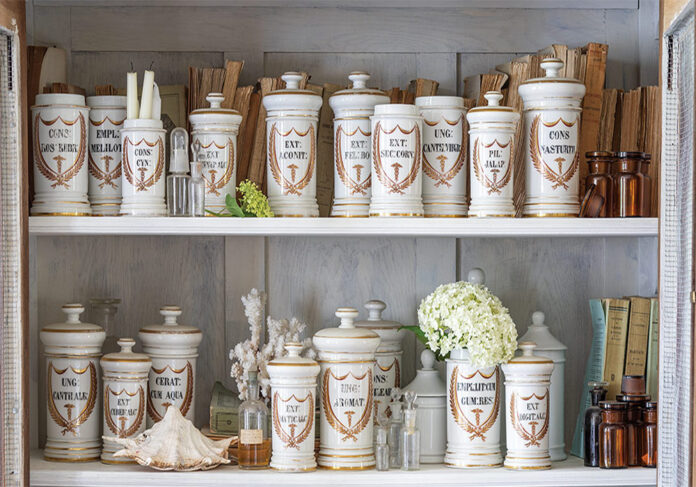 A collection of French apothecary jars is displayed on a shelf among sweet flowers and seashells.