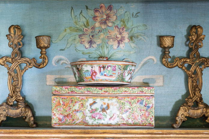 Rose medallion mantle pieces against a floral background, paired with antique candle sticks.