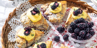 Blackberry-Thyme Scones nestle around a bowl of fresh blackberries. The pastries rest on a whicker tray, dappled in lace and red gingham.