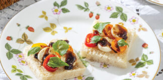 Colorful cherry tomatoes with mozzarella and basil bedeck pillowy white bread on china decorated in strawberries and green leaves.