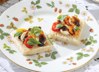 Colorful cherry tomatoes with mozzarella and basil bedeck pillowy white bread on china decorated in strawberries and green leaves.