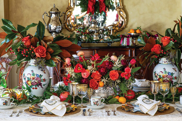 A formal dining room finds itself the scene of vibrant Christmas splendor, including bright blossoms, magnolia leaves, and porcelain painted with the fruits of the season.