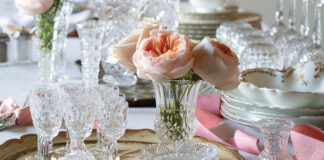 A collection of crystalware is placed atop the table for cleaning, but the work is made into a lovely display with sprays of fresh pink peonies and curls of ribbon.