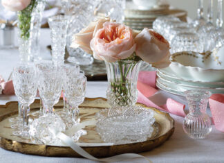 A collection of crystalware is placed atop the table for cleaning, but the work is made into a lovely display with sprays of fresh pink peonies and curls of ribbon.