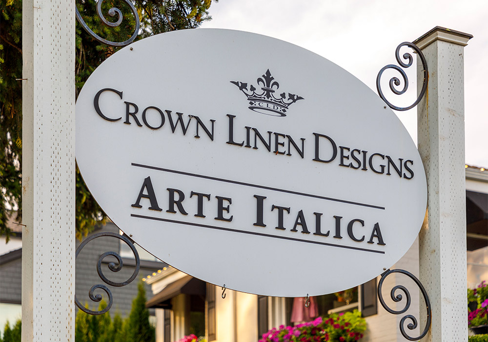 White cabinet display filled with Arte Italica chinaware and glassware and Crown Linen Designs linens. 