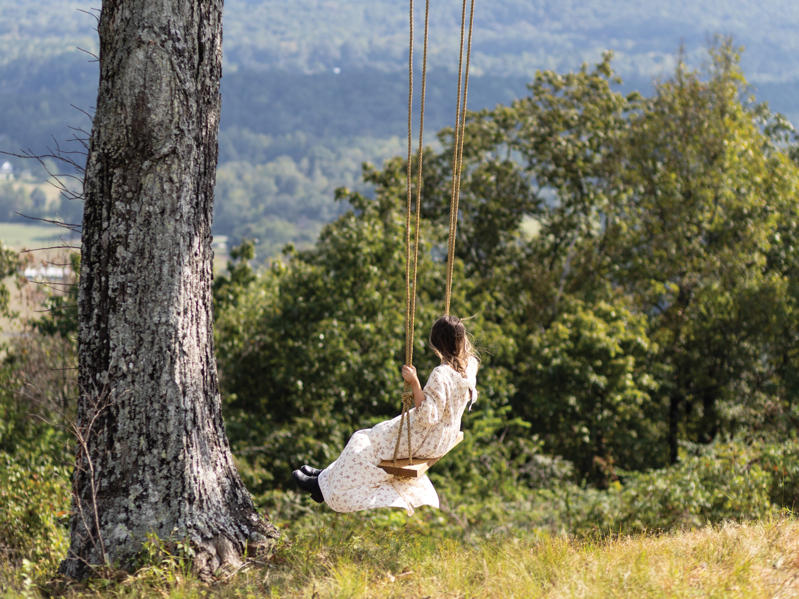 Girl in dress swinging on an outdoor swing
