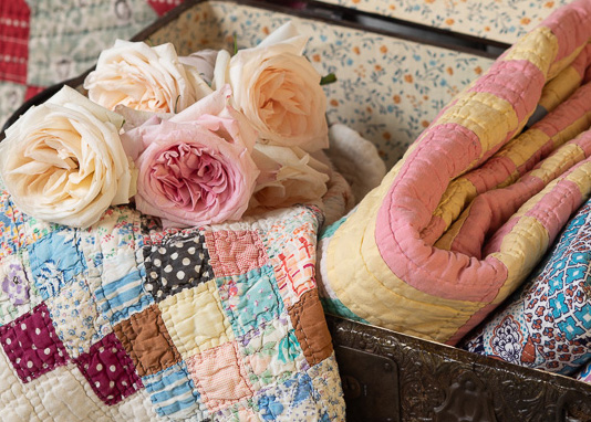 Quilts folded in a vintage chest with a bouquet of roses