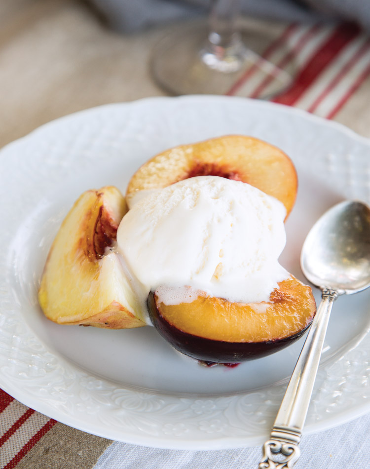 A scoop of ice cream begins to melt over freshly roasted stone fruit.