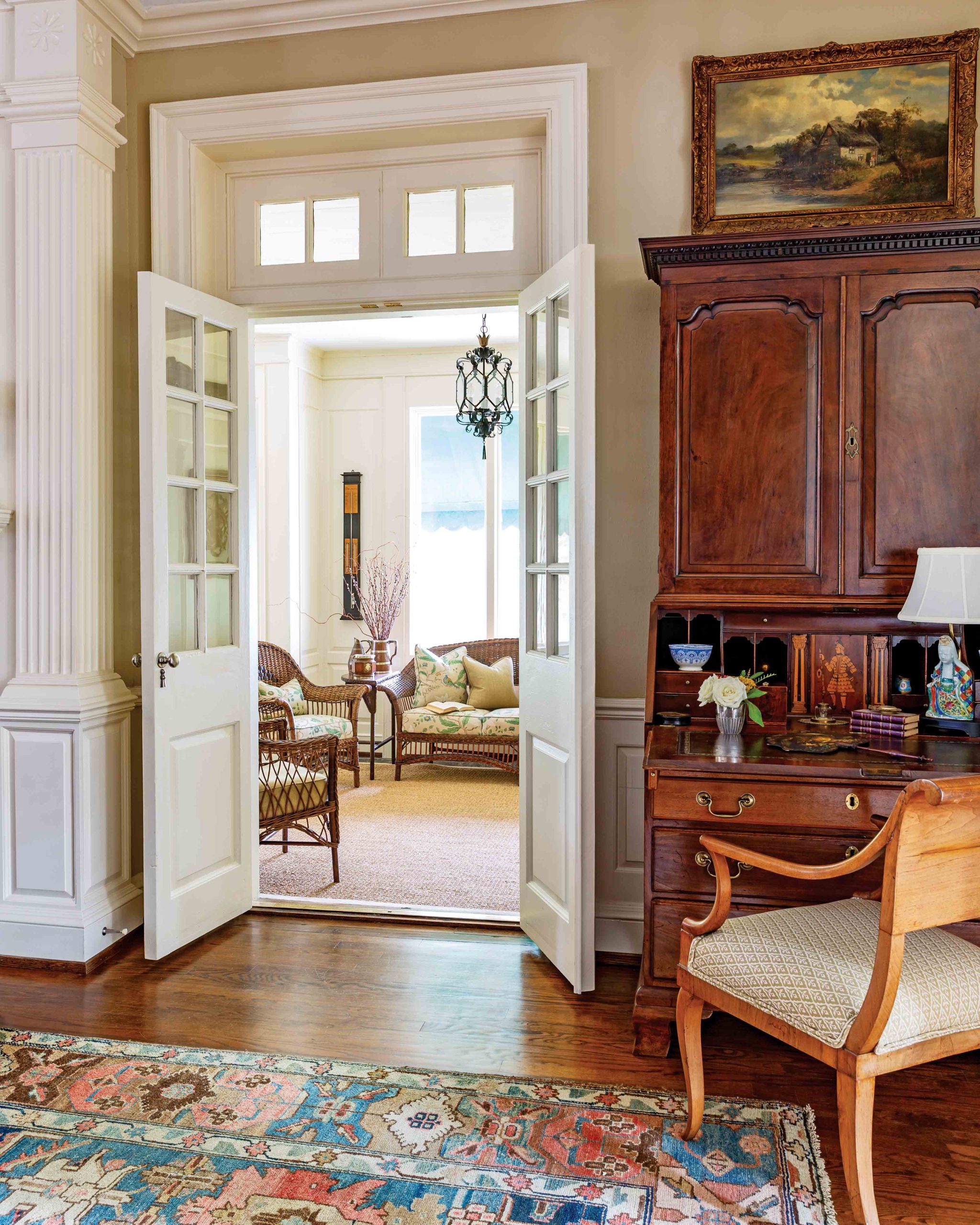 From the workspace at this wooden desk through the doorway a sitting room is seen.
