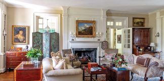An antique-filled living room boasts rich woods and warm hues set against a cream-and-white backdrop.