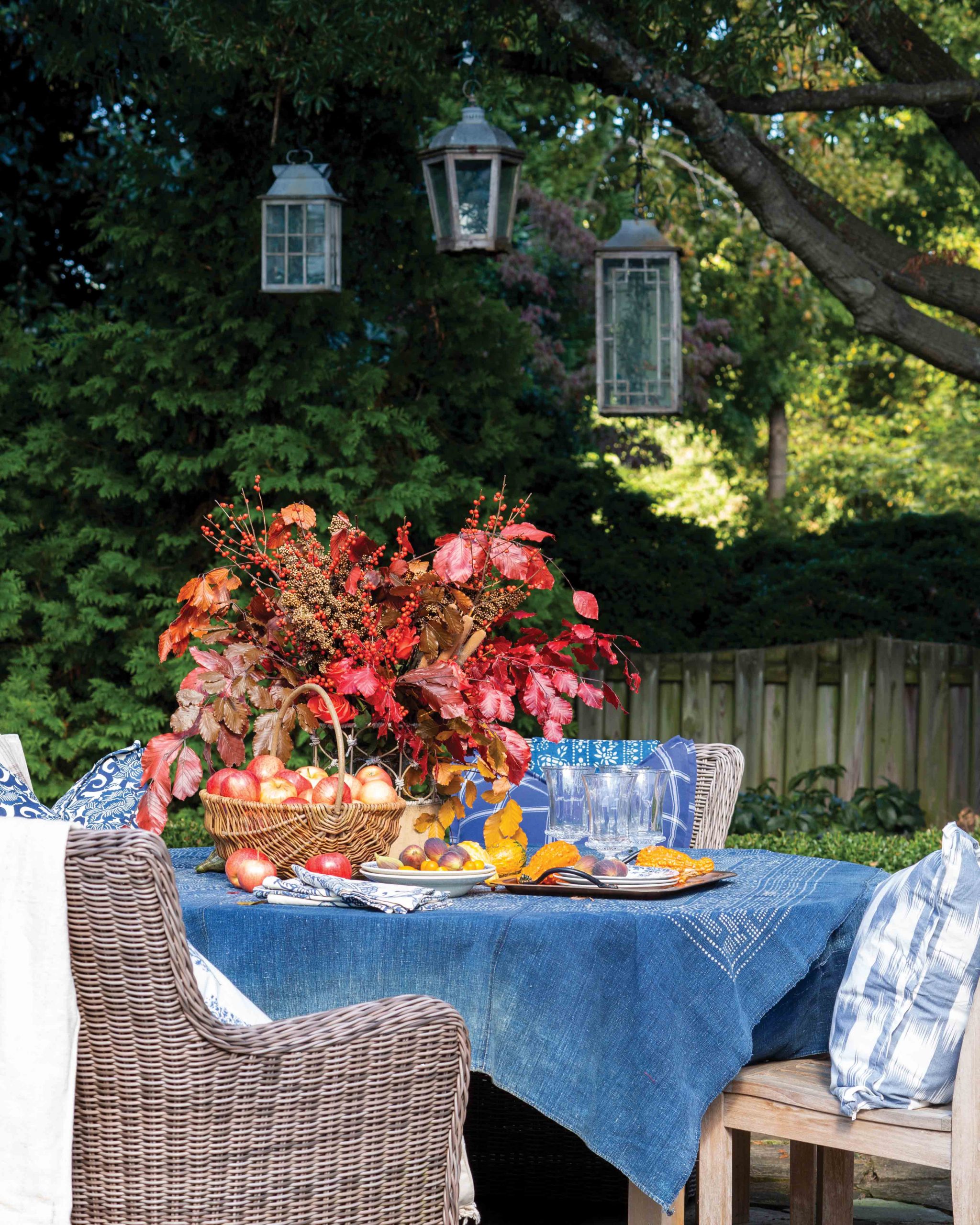 Below hanging lanterns, a backyard table is set with a leafy centerpiece.