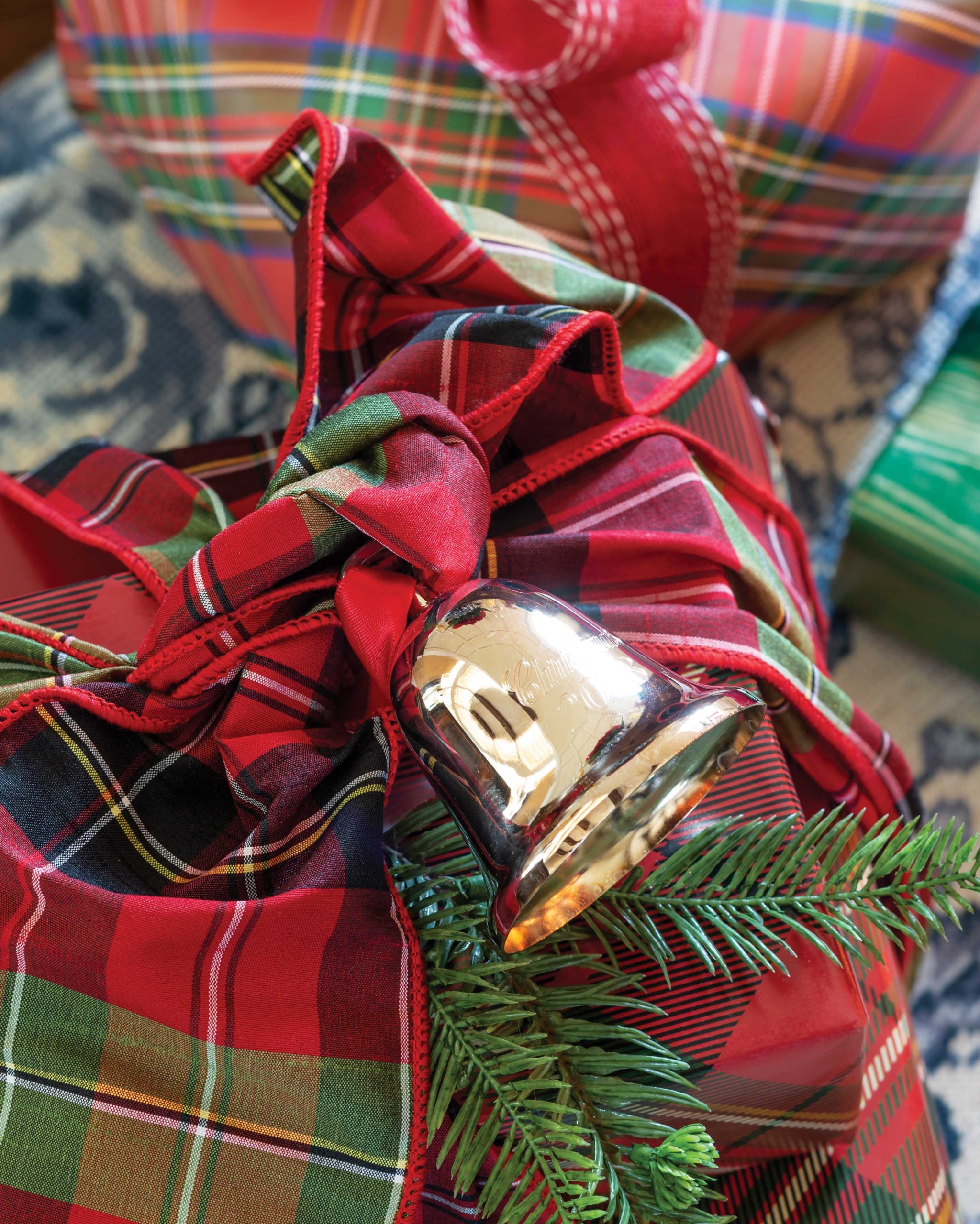 A silver bell ornament is tied with plaid ribbon to a gift.