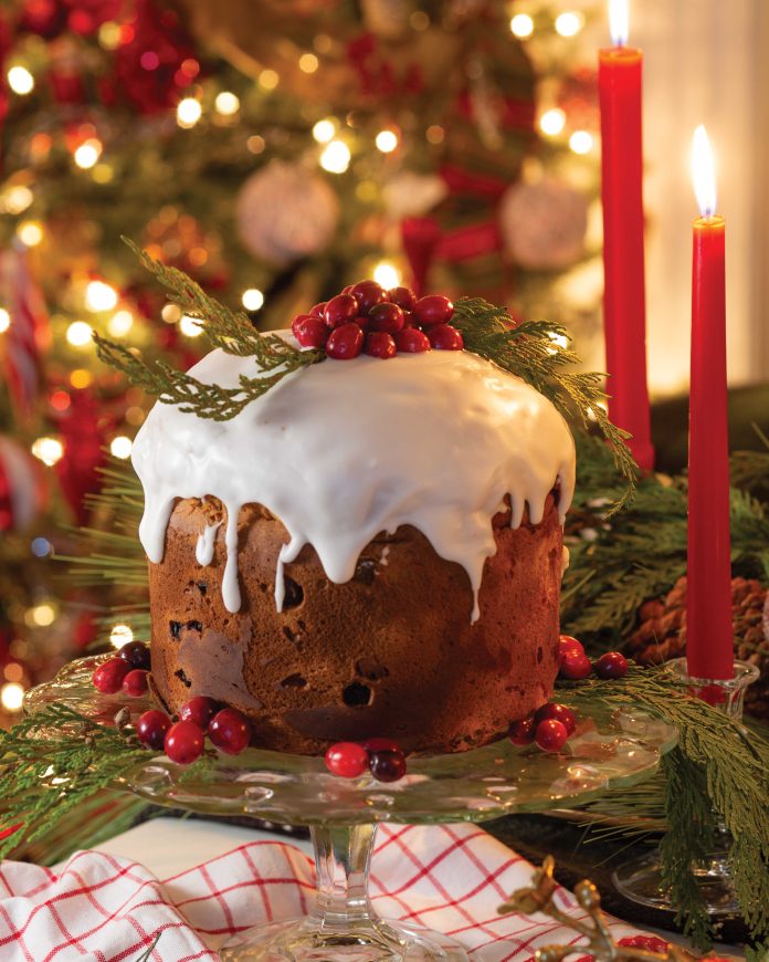 The focal point of a Christmas scene is panettone topped with homemade glaze, bright red berries, and sprigs of greenery.