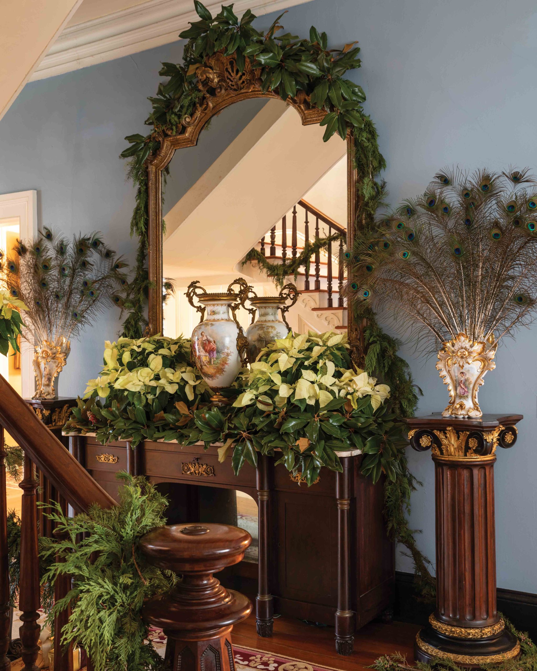 A large mirror rests atop a marble-top sideboard, which holds a rare antique urn and a dozen white poinsettias