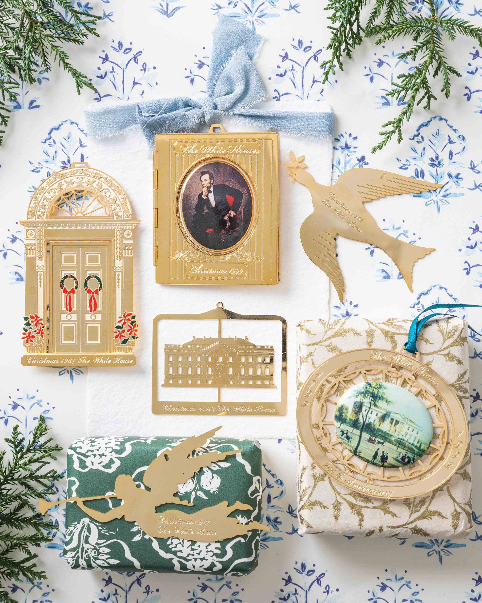 An assembly of six ornaments from this White House Christmas collection includes the 1999, 1992, 1987, 1983, 1982, and original 1981 varieties set against a blue-and-white wrapping paper background.