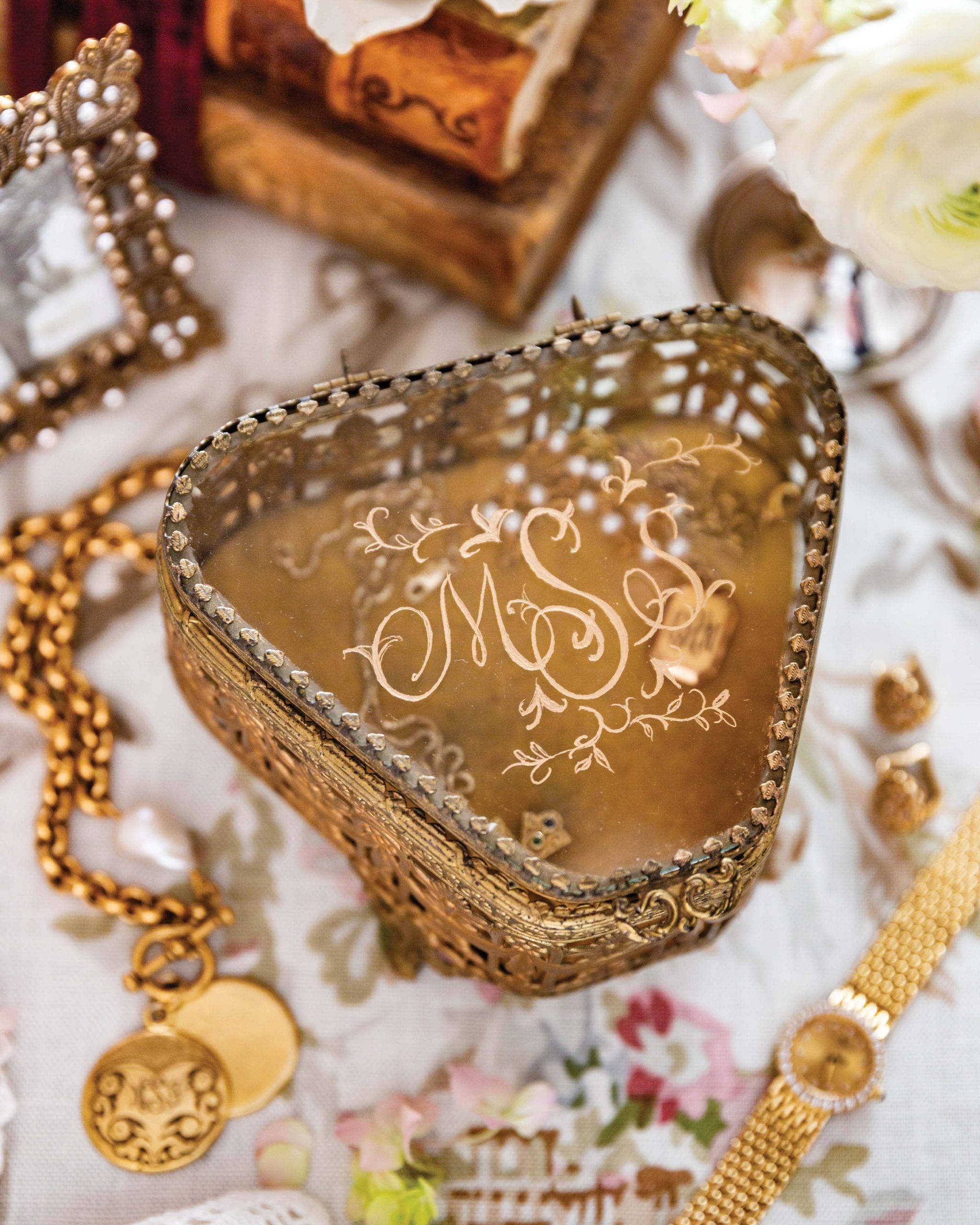 A triangle-shaped gold and glass jewelry box features a beautifully carved monogram that reads “M. S. S.”