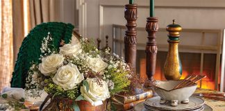 A stack of rustic plates, time-worn candlesticks, and a cache of snowy rosebuds dress the table in coziness.