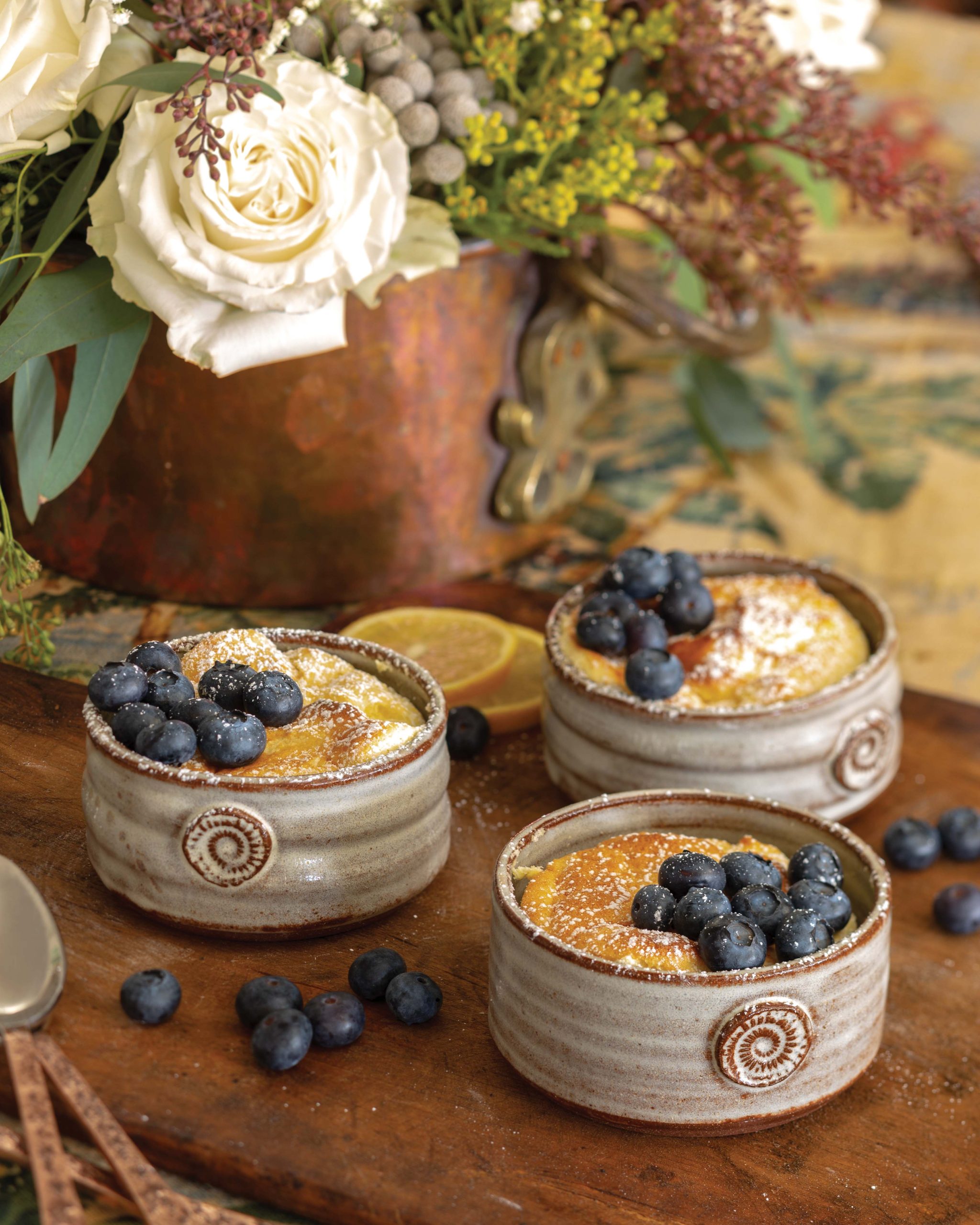 Baked in rustic pottery as individual dishes, Meyer Lemon Pudding Cake is topped with fresh blueberries and confectioners’ sugar.