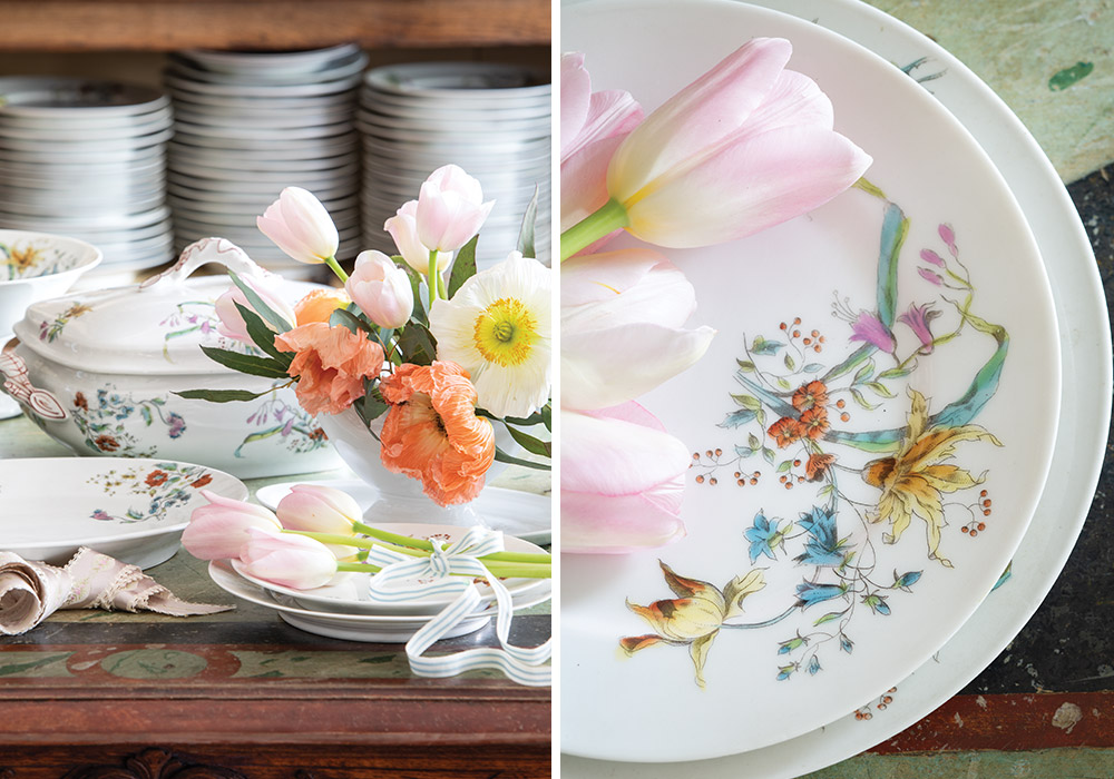 A collection of white Limoges plates dressed in floral artistry are displayed beside tulips and other spring blossoms.
