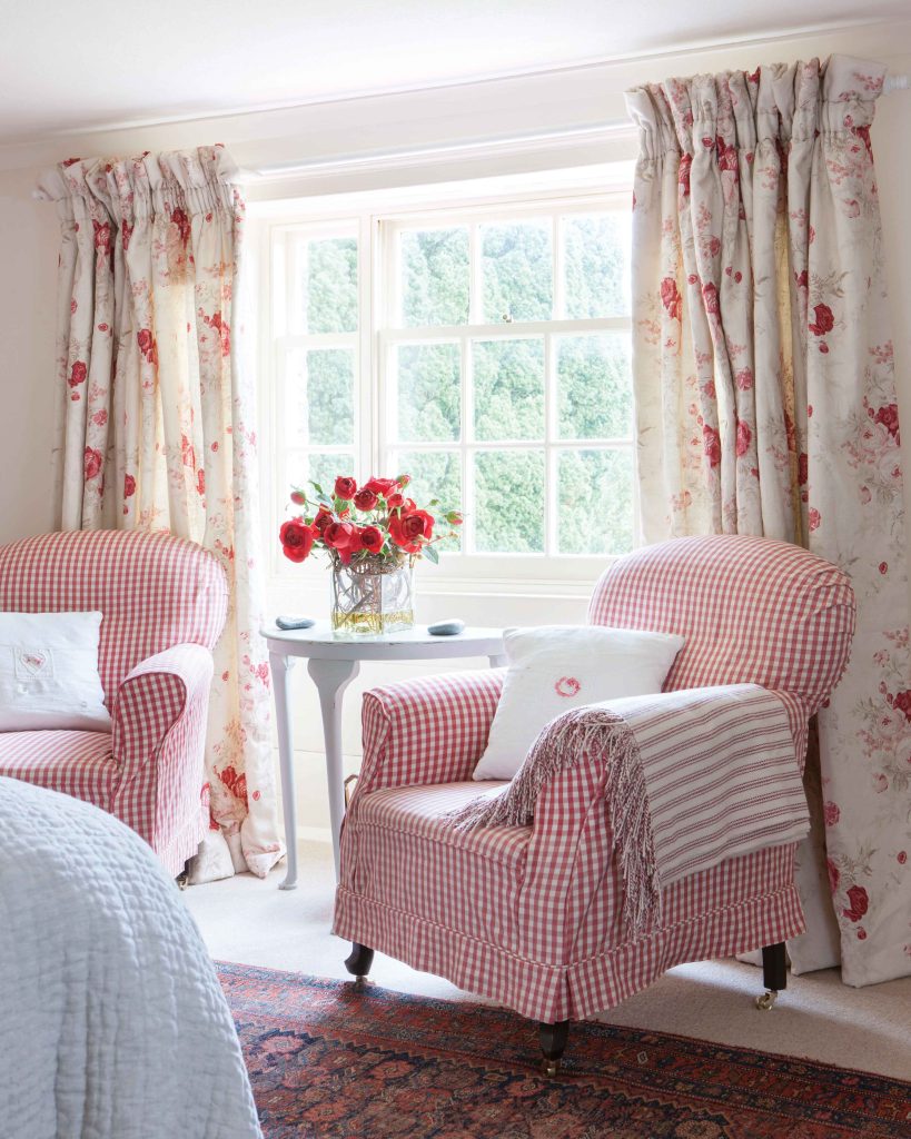 Two red gingham armchairs sit beside a bright window, dressed in floral fabrics that seem to coordinate perfectly with the bouquet that sits on the side table.