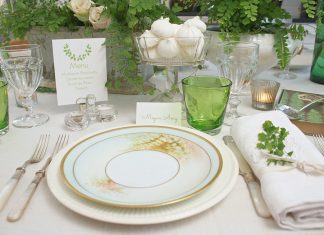 A place setting of white and green awaits a friendly gathering, with sweet twigs of foliage tucked into the napkin and fern imagery on the plates and papers.