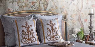 A breathtaking French bed is set against French Market Collection wallpaper and dressed in the brand’s antique motif pillows.