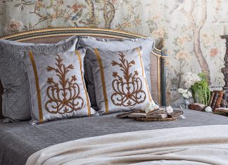 A breathtaking French bed is set against French Market Collection wallpaper and dressed in the brand’s antique motif pillows.