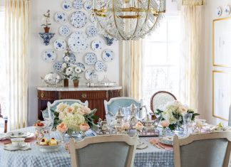 A rectangular dining table in Nicola Bathie McLaughlin’s Texas home displays a blue-and-white checked tablecloth, colorful china, and bouquets of pastel flowers.