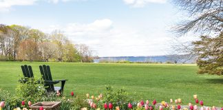 Two slender Adirondack chairs sit at the edge of a tulip garden and a verdant field, looking out onto the bay.