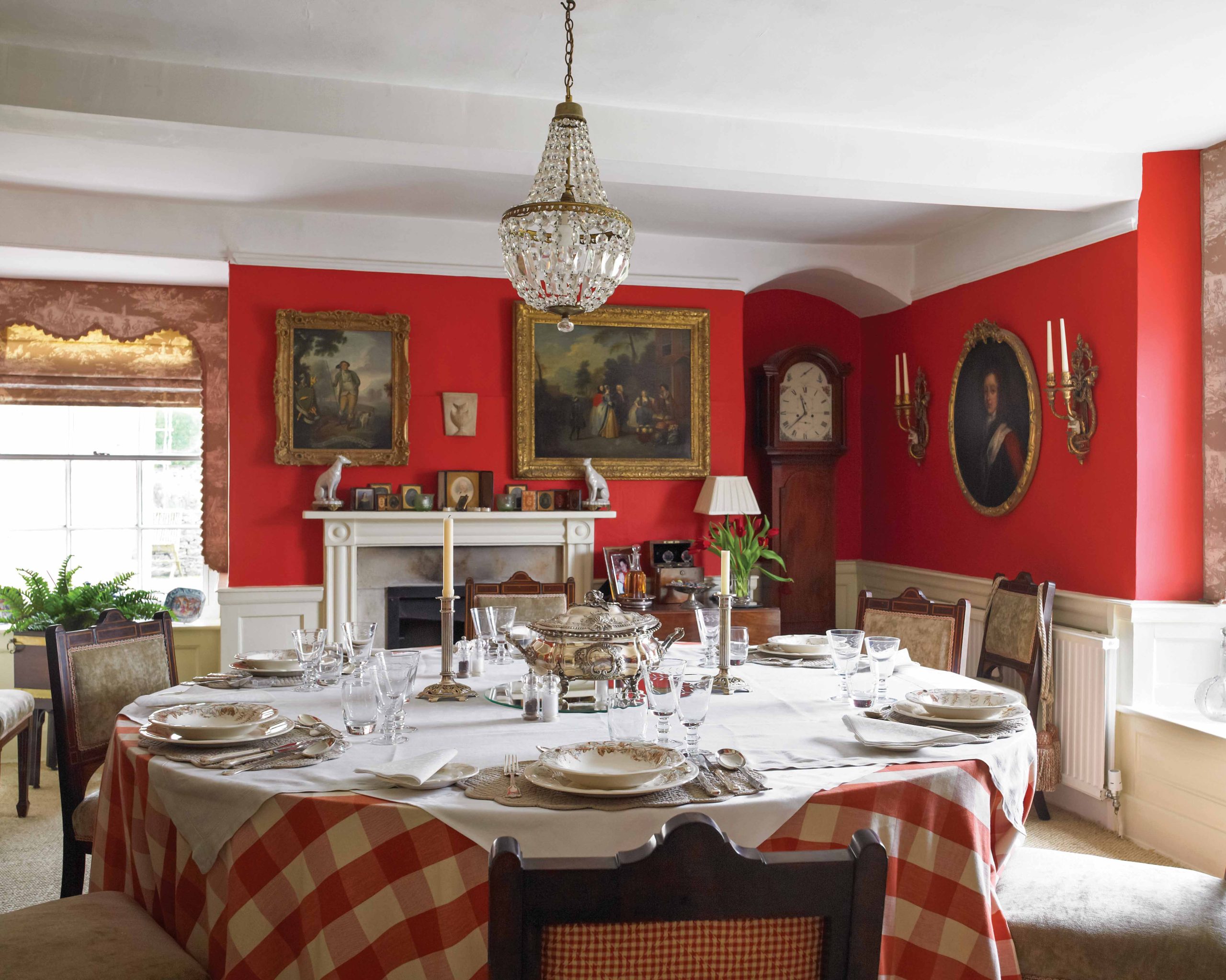 Vibrant red walls, ornate gold frames, and a large round table in this dining area exude formal beauty.