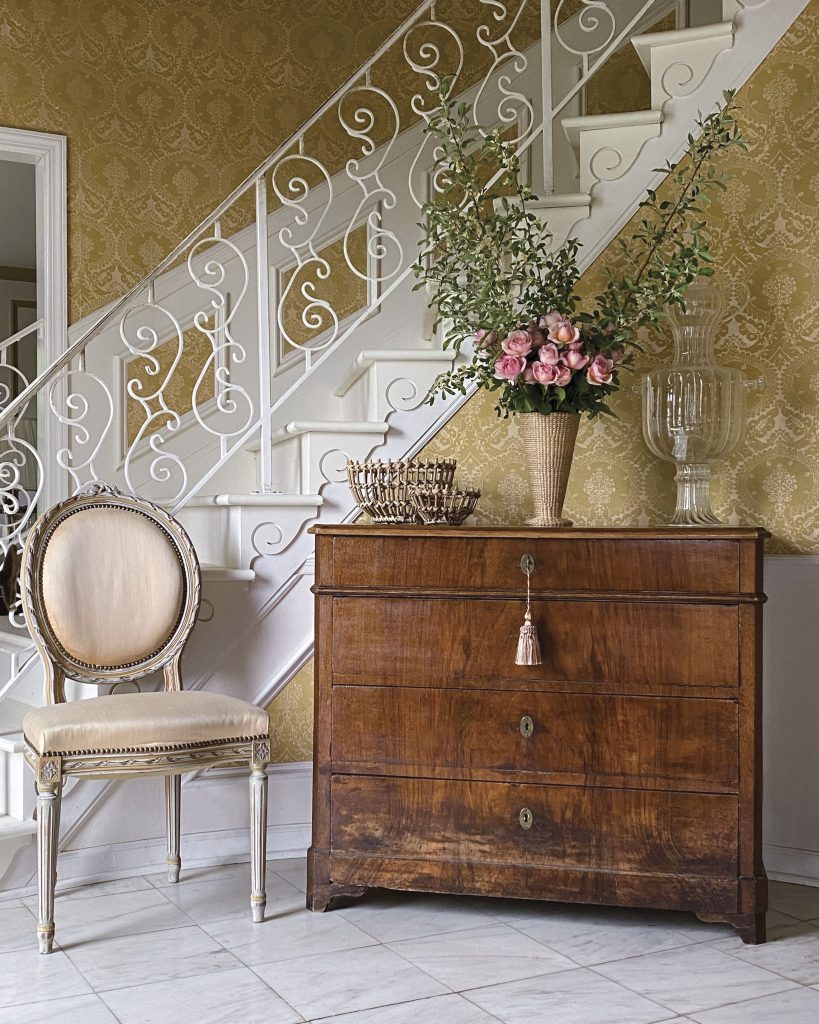 A reproduction Louis XVI chair sits beside a French chest in the front entry hall at Tallwood.