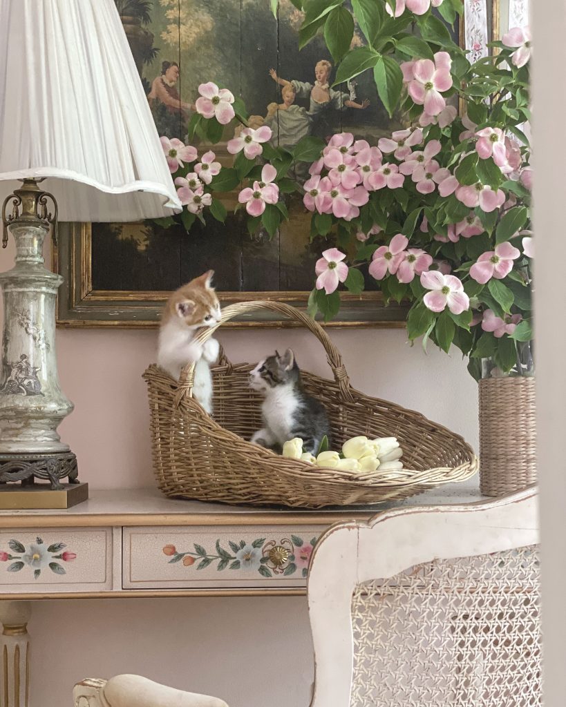 A pair of kittens play in a basket in front of an antique oil on boards after Jean-Honoré Fragonard’s The Pursuit.