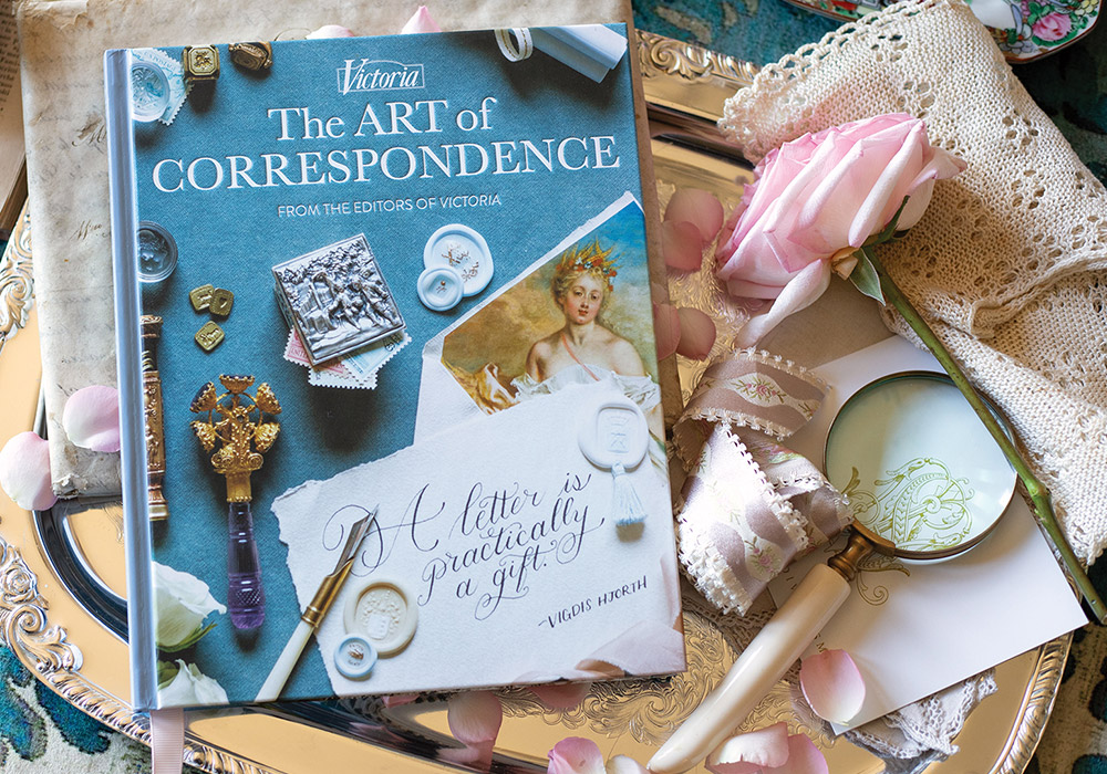 The Art of Correspondence on golden tray with pearl-handled magnifying glass and pink rose.