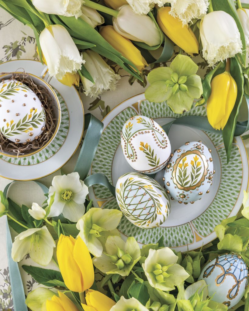 A mingling of intricately decorated Easter eggs sits atop a Herend plate surrounded by tulips and other blossoms.