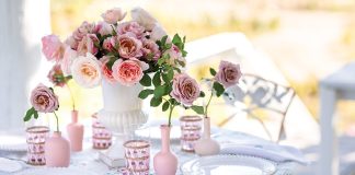 A bouquet of roses sits at the center of a table laden with breezy white linens in an outdoor setting.