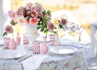 A bouquet of roses sits at the center of a table laden with breezy white linens in an outdoor setting.