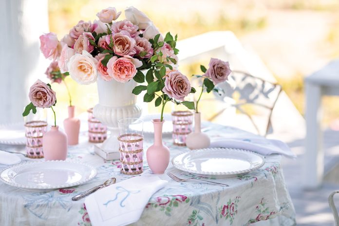 A bouquet of roses sits at the center of a table laden with breezy white linens in an outdoor setting.
