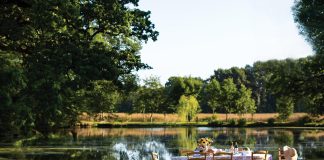 In a grassy clearing beside a sparkling lake, a breezy table is set for summer dining