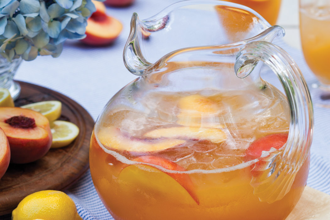 Glass pitcher filled with Peach Lemonade and slices of fresh peaches.