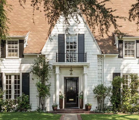 Lush vegetation welcomes guests to Leslie Saeta’s white shingled house in Southern California. A black front door and matching shutters are classic design elements that complement this early twentieth-century home.