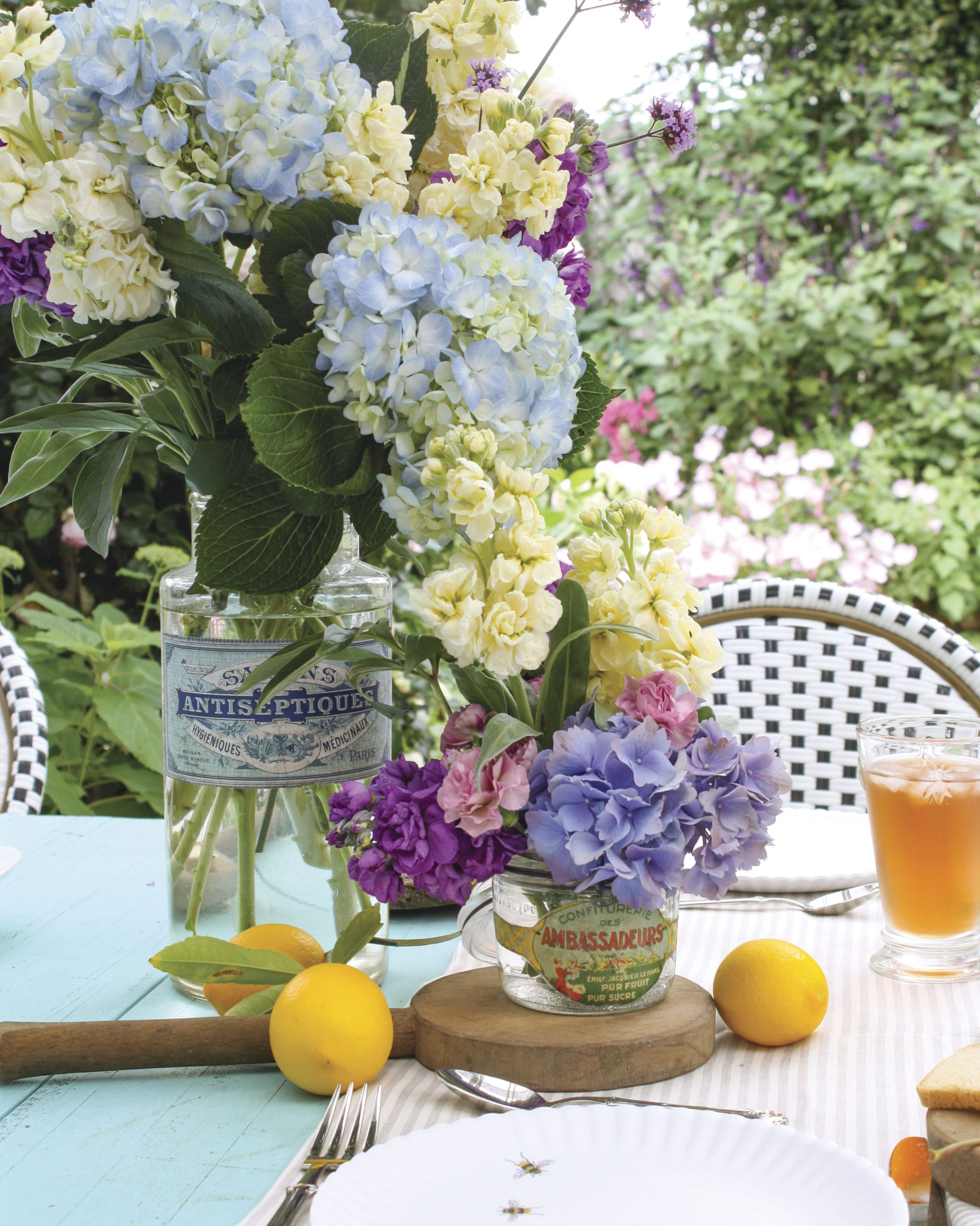 In a sunny outdoor space, a bright blue table is set with a casual bouquet placed in an antique French jar.