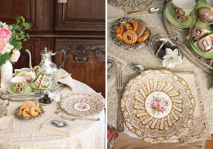 A small table is draped in antique French lace, set for an intimate tea for two. The silver tray holds priceless porcelain cups and saucers bearing feminine portraits.