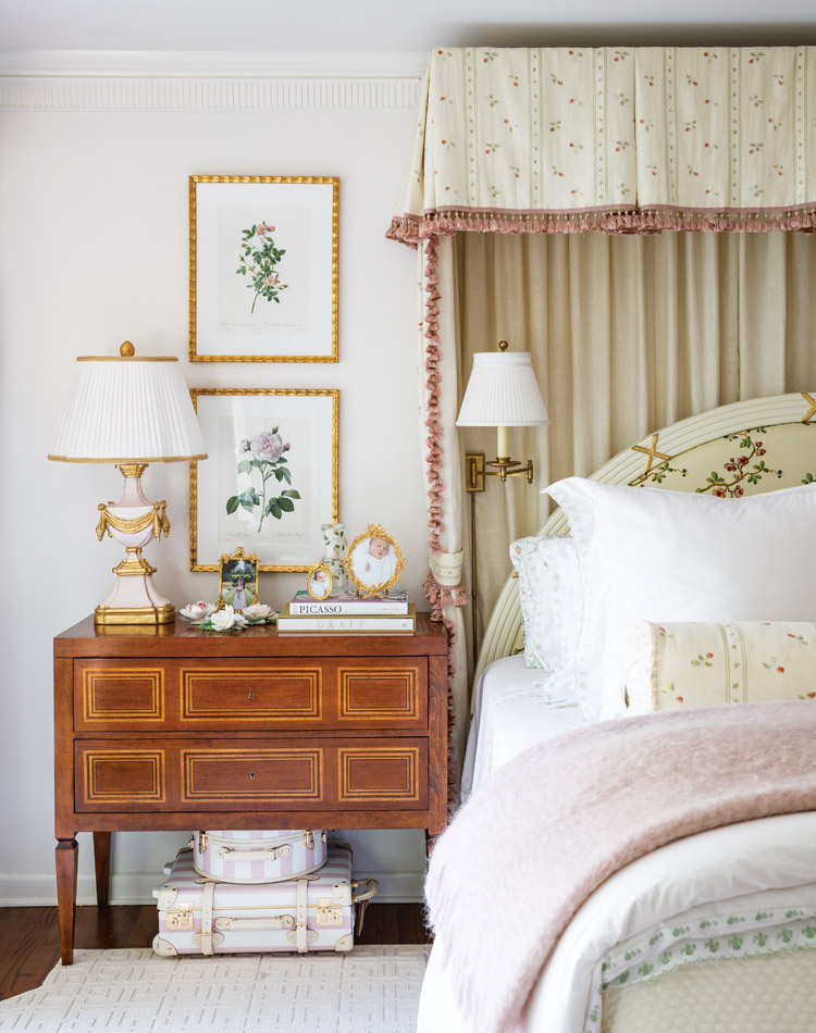 Nicola Bathie McLaughlin’s primary bedroom is a continuance her feminine style. Touches of soft pink find their way to the bed linens, antique French lamp on the glossy wood bedside table, and framed pink botanical hanging on the wall.