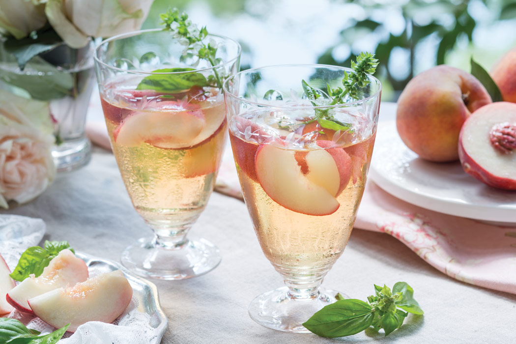 White Peach Sangria in glasses garnished with peach slices and basil.
