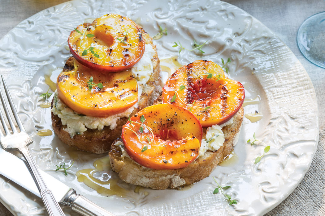 Plate of two open-Faced Sandwiches with light-colored cheeses topped with grilled peaches.