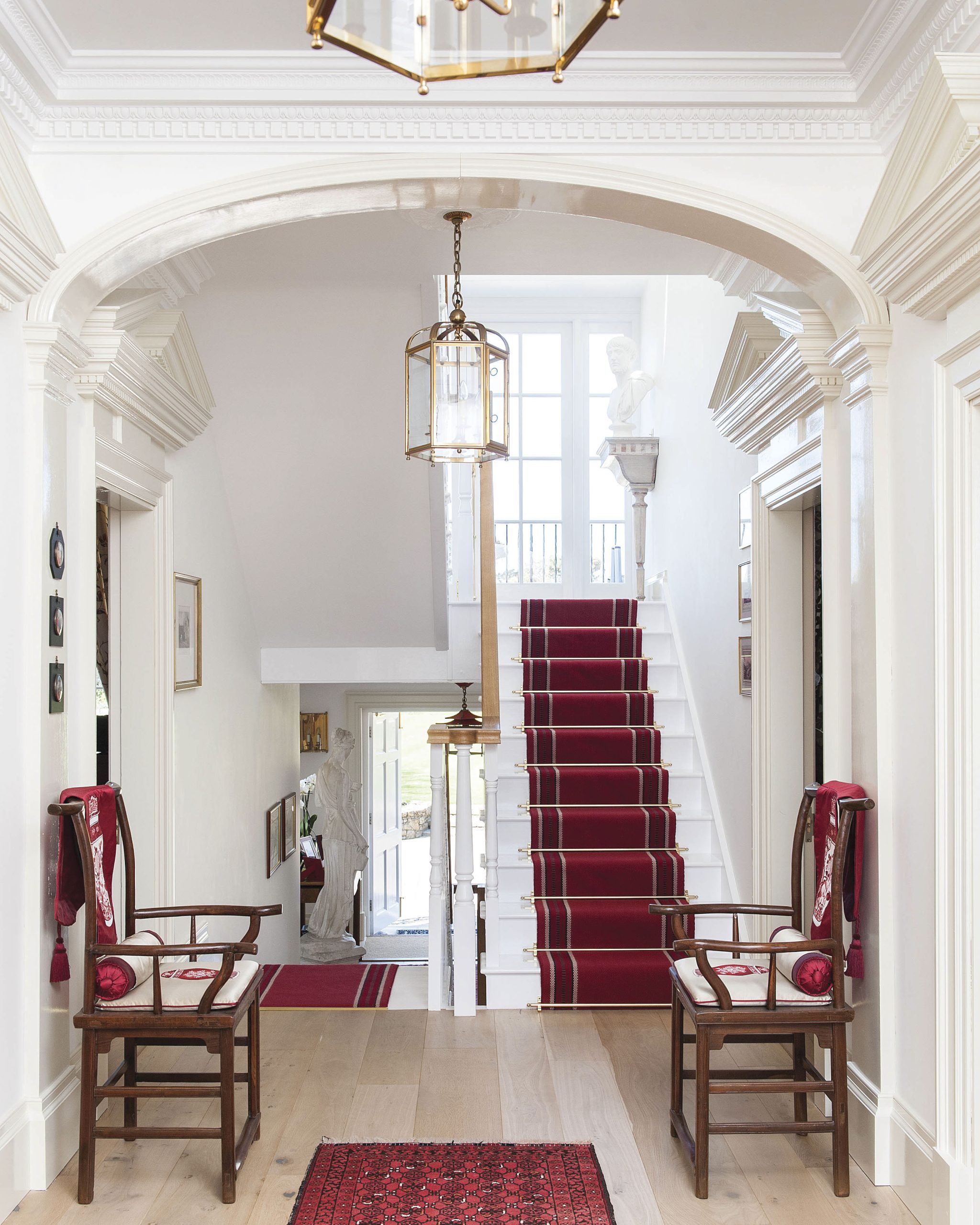 The staircase is bathed in natural light and draped in vibrant red stair runner, kept in place with brassy carpet rods.