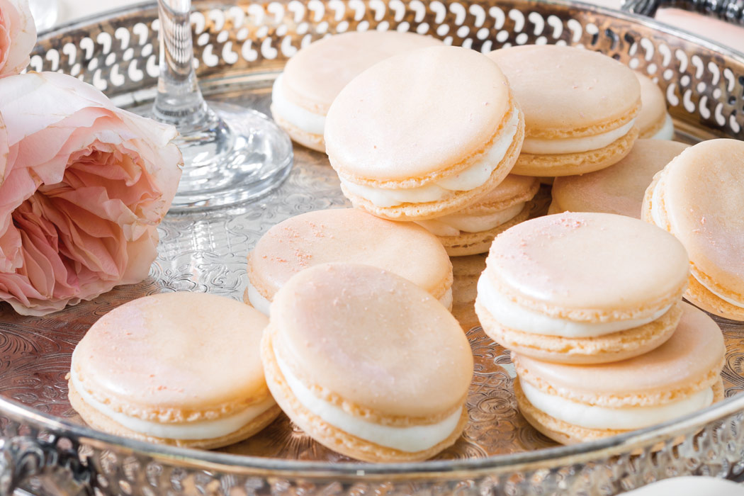 A silver tray filled with light pink Amaretto-Peach Macarons and flowers.