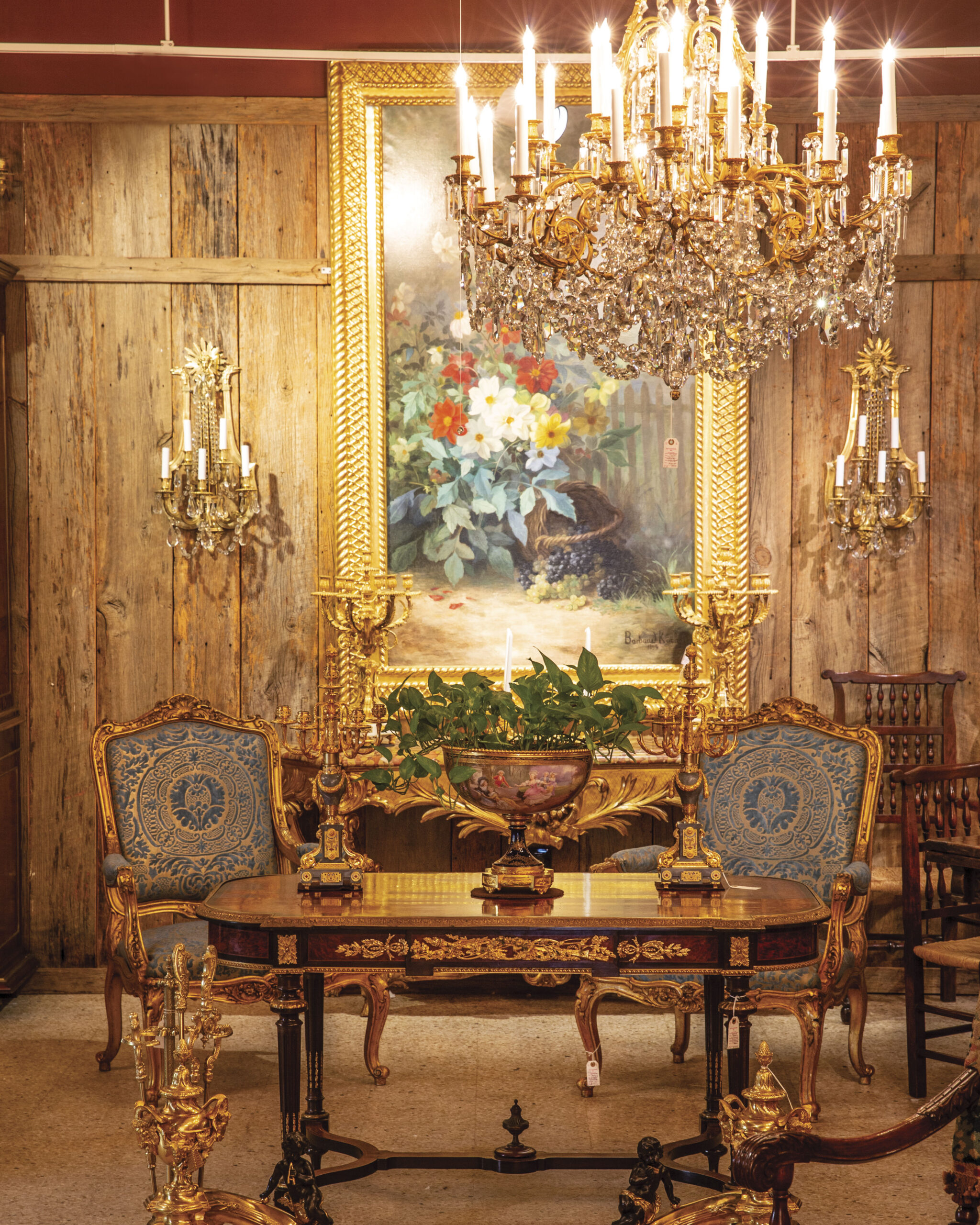 A pair of matching chairs sit on either side of a splendorous table, lit by the glow of a grand chandelier.