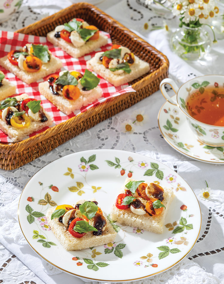 Colorful cherry tomatoes with mozzarella and basil bedeck pillowy white bread on china decorated in strawberries and green leaves.